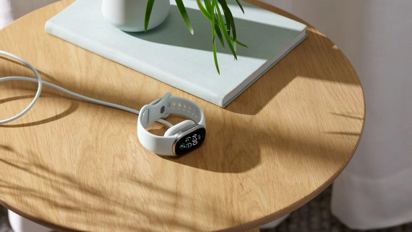 Google Fitbit Edge with a light band on a wooden side table beside its charging cable