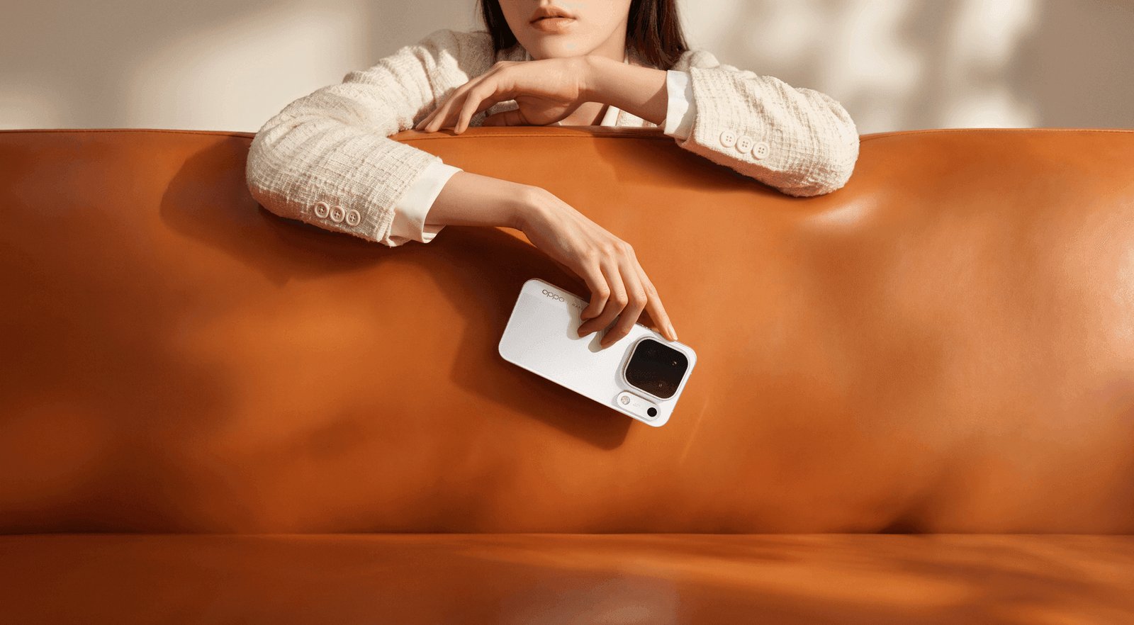 Woman leaning on a tan leather sofa holding the OPPO Find X10 Pro Max in Luna White