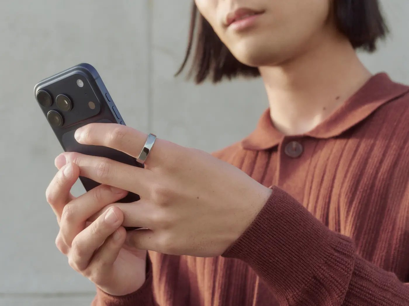 Person wearing a silver Oura ring while using a smartphone