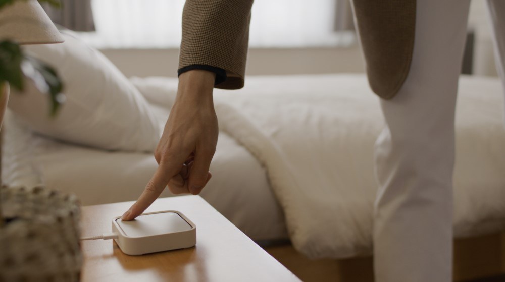 Person pressing the Smart Button on a SmartThings Station hub on a bedside table
